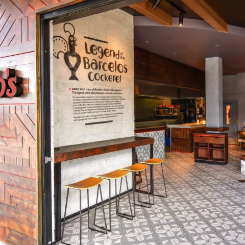 Geometric timber facade, illuminated red restaurant signage, stenciled concrete wall, industrial counter stools, patterned floor tiles, modern hospitality entryway.