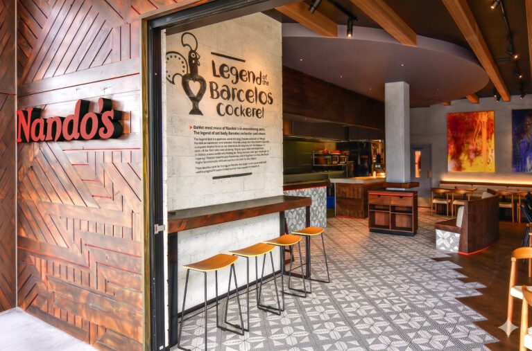 Geometric timber facade, illuminated red restaurant signage, stenciled concrete wall, industrial counter stools, patterned floor tiles, modern hospitality entryway.