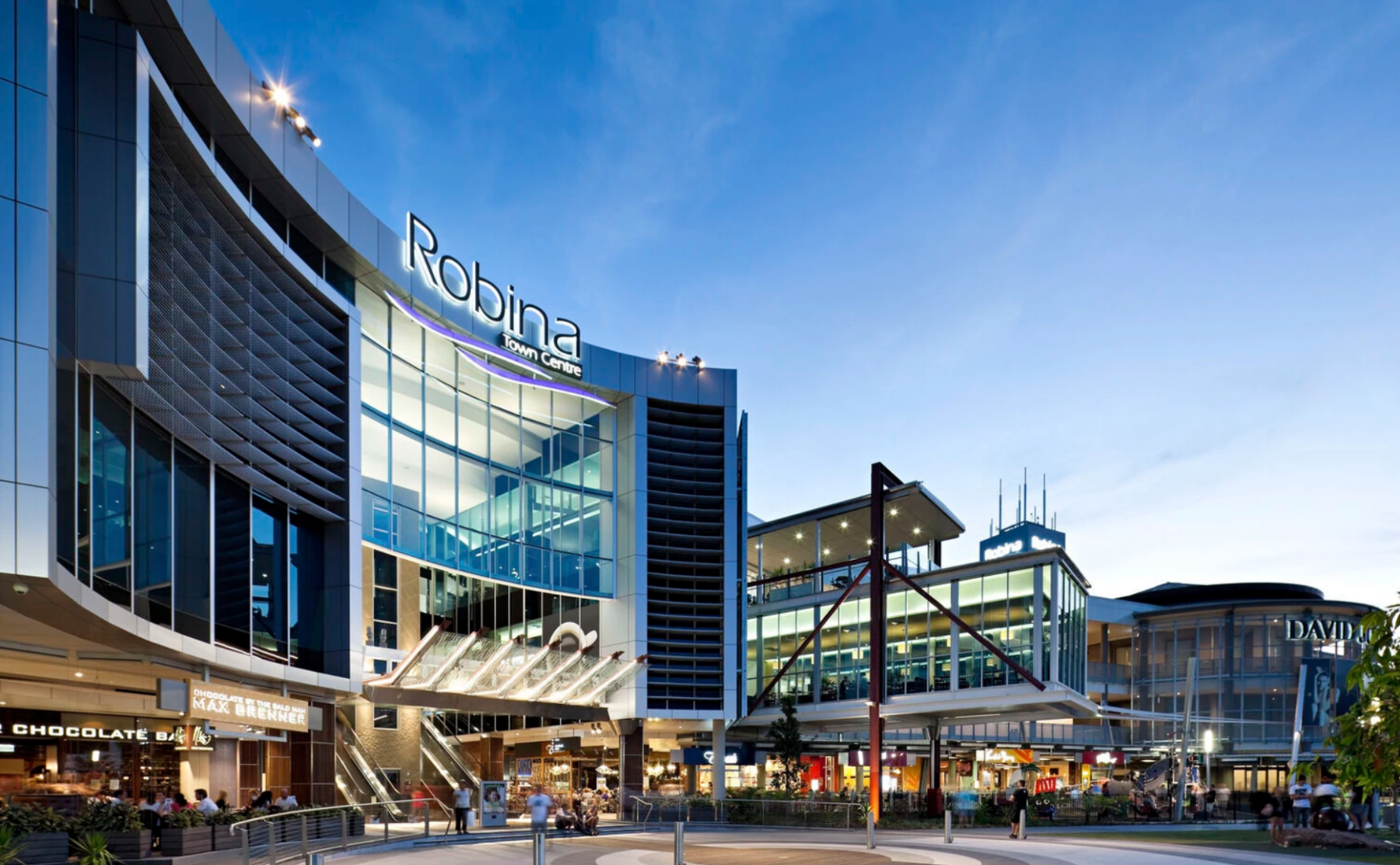 A sweeping curved glass facade framing a multi-level entrance plaza and escalators.