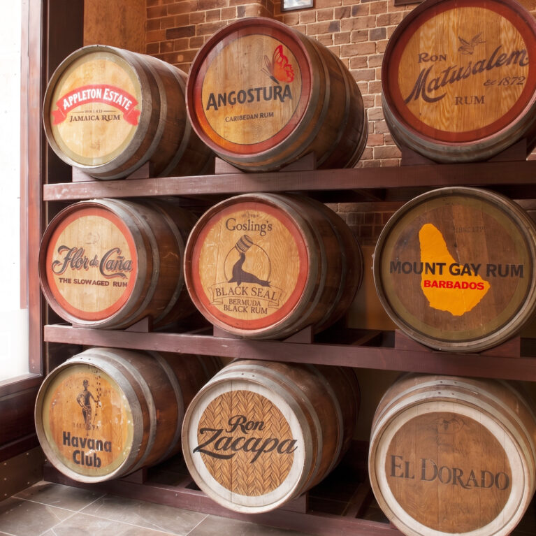 Oak rum barrels, custom cellar racking, branded barrel heads, exposed heritage brick, stone floor tiles, commercial hospitality joinery, vintage product display, thematic restaurant interior.