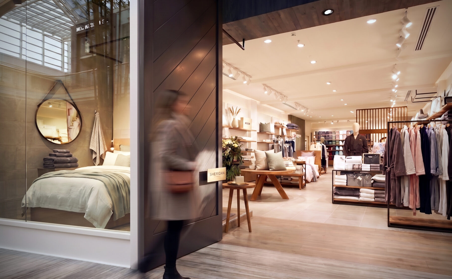Premium retail entrance, sliding timber door, glass display window, mock bedroom staging, timber look flooring, directional track lighting, luxury apparel rails.
