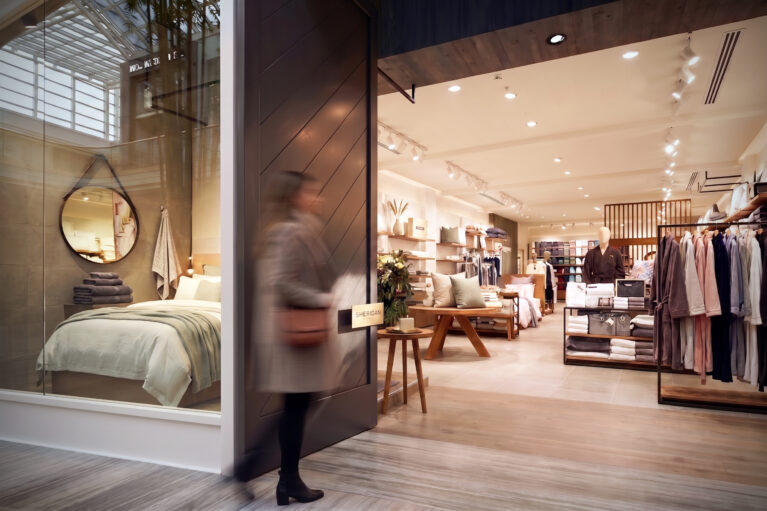 Premium retail entrance, sliding timber door, glass display window, mock bedroom staging, timber look flooring, directional track lighting, luxury apparel rails.