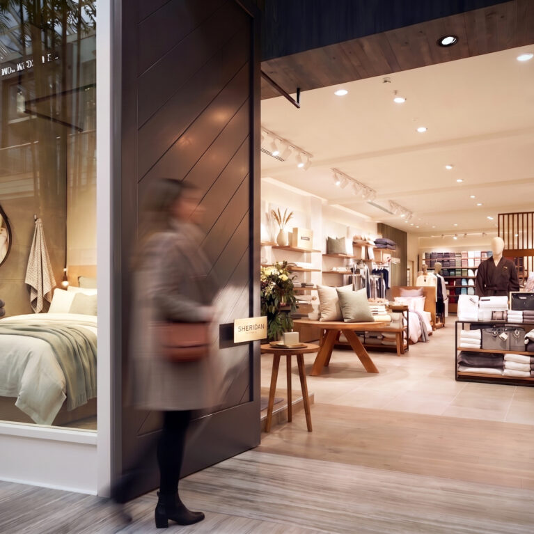 Premium retail entrance, sliding timber door, glass display window, mock bedroom staging, timber look flooring, directional track lighting, luxury apparel rails.