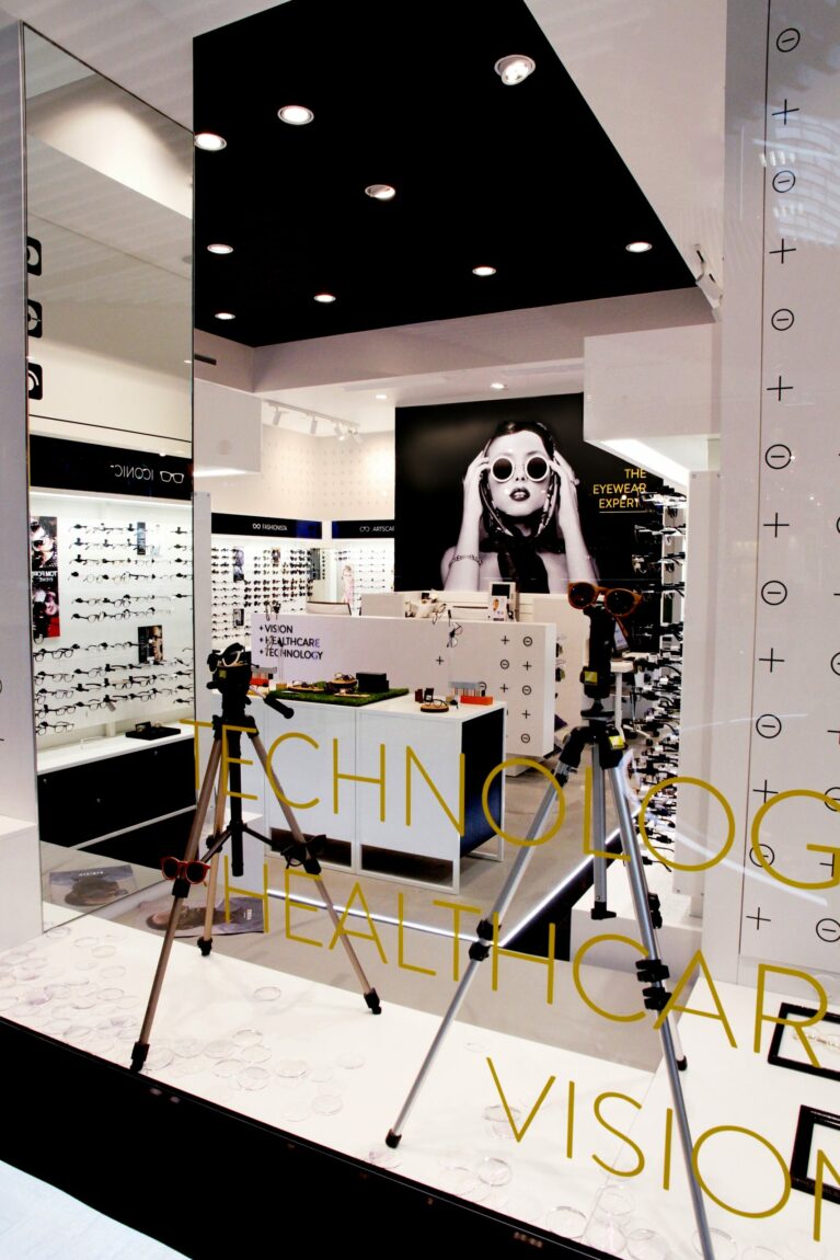 Window display design, optical measuring equipment, marble laminate base, gold glass lettering, structural mirrored column, dropped acoustic ceiling, interactive consultation suite, clinical retail interior.