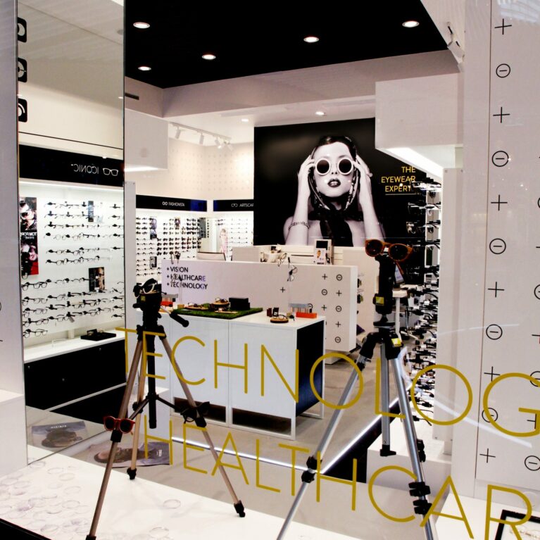 Window display design, optical measuring equipment, marble laminate base, gold glass lettering, structural mirrored column, dropped acoustic ceiling, interactive consultation suite, clinical retail interior.
