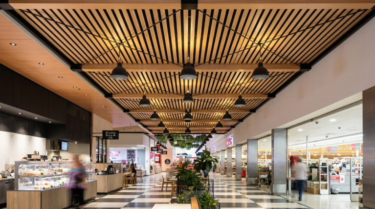 Timber batten ceiling, linear pendant lighting, checkered terrazzo floor, open shopfront thresholds, fresh food precinct layout, commercial mall corridor, public seating nodes.