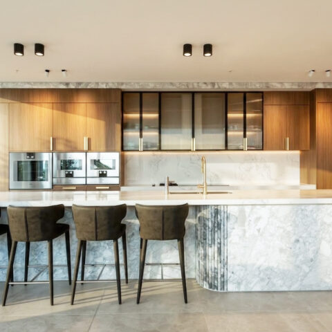 The kitchen exudes luxury and functionality, featuring a Calacatta marble island and light oak cabinetry. Black accents and integrated appliances enhance the modern aesthetic, while soft lighting highlights the refined textures of the materials.