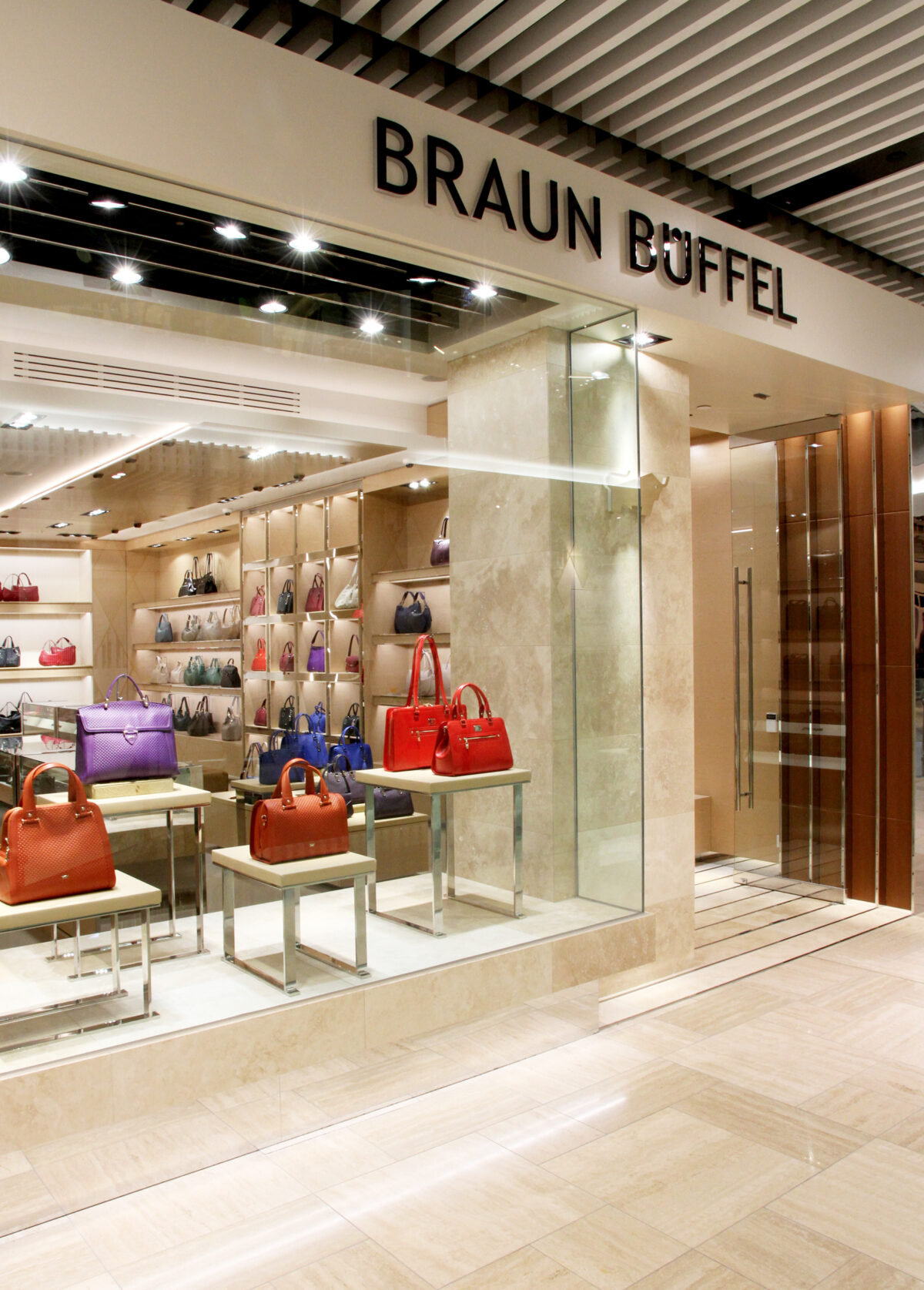 Luxury retail facade, glass storefront partition, dimensional building signage, travertine limestone cladding, timber ceiling slats, window display pedestals, polished steel door handles.