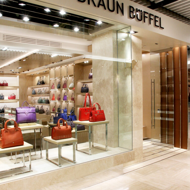 Luxury retail facade, glass storefront partition, dimensional building signage, travertine limestone cladding, timber ceiling slats, window display pedestals, polished steel door handles.