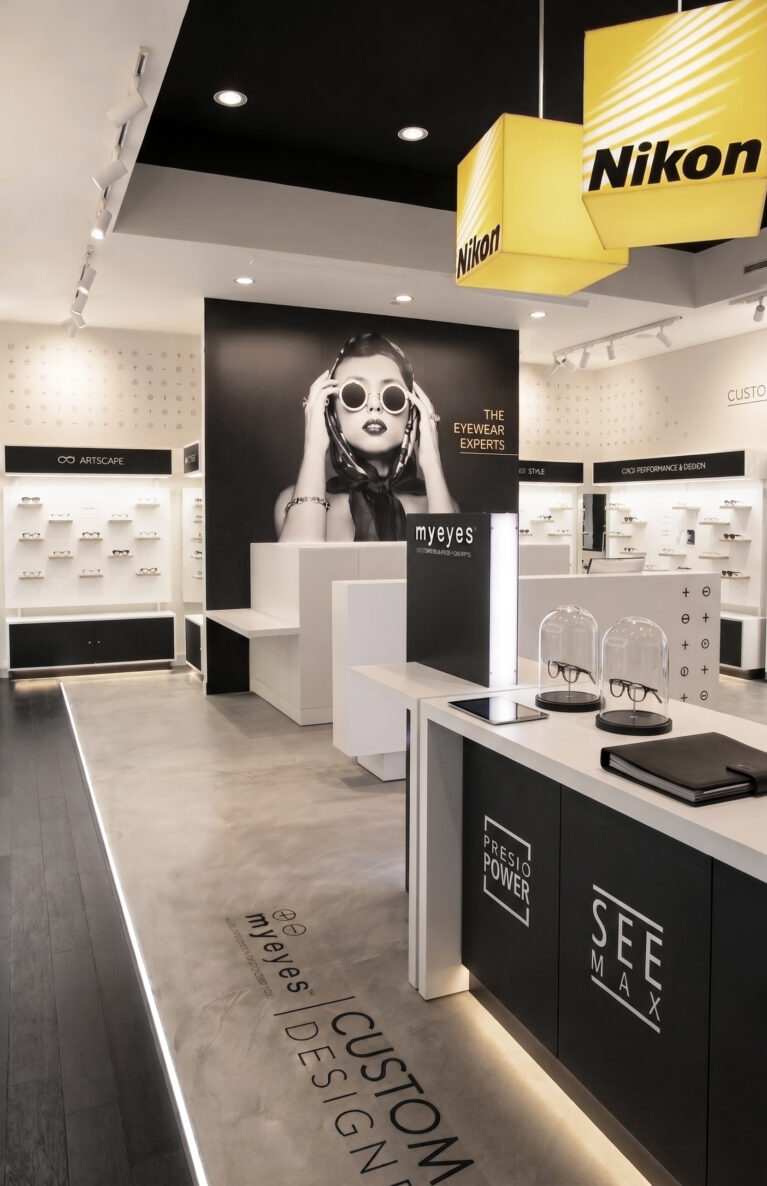 Optical boutique interior, custom lens bar, concrete floor transition, illuminated floor track, large scale super-graphic, backlit eyewear displays, hanging lightbox signage, black acoustic ceiling