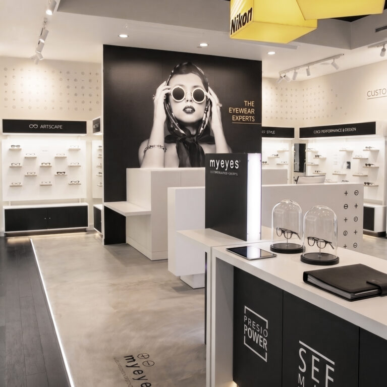 Optical boutique interior, custom lens bar, concrete floor transition, illuminated floor track, large scale super-graphic, backlit eyewear displays, hanging lightbox signage, black acoustic ceiling