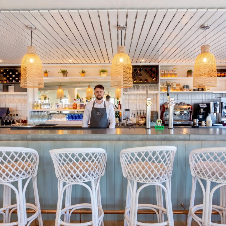 Linear bar counter featuring woven wicker pendants and woven-backed stools.