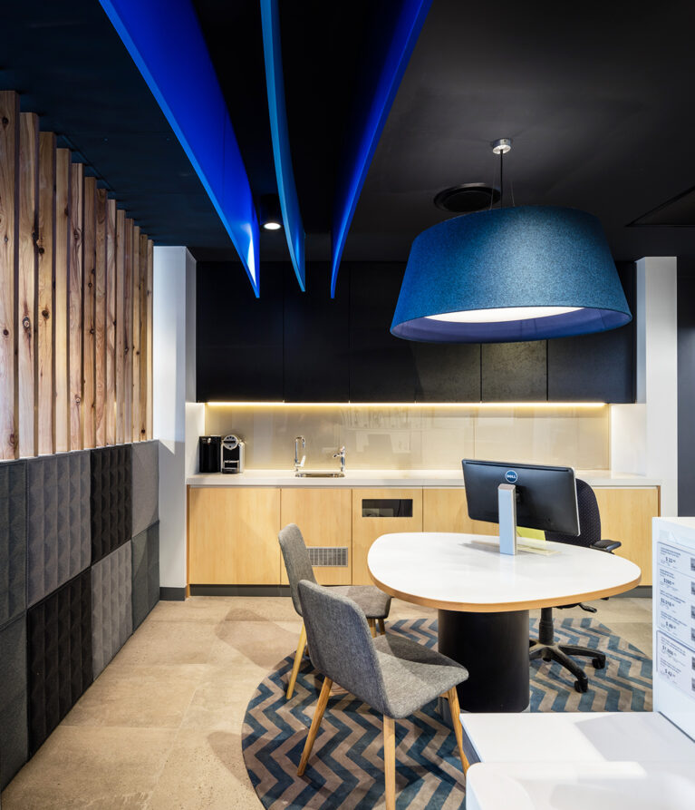 Corporate consultation workspace, acoustic ceiling baffles, oversized felt pendant lamp, chevron pattern rug, natural timber wall cladding, grey fabric acoustic wall panels, light oak cabinetry.