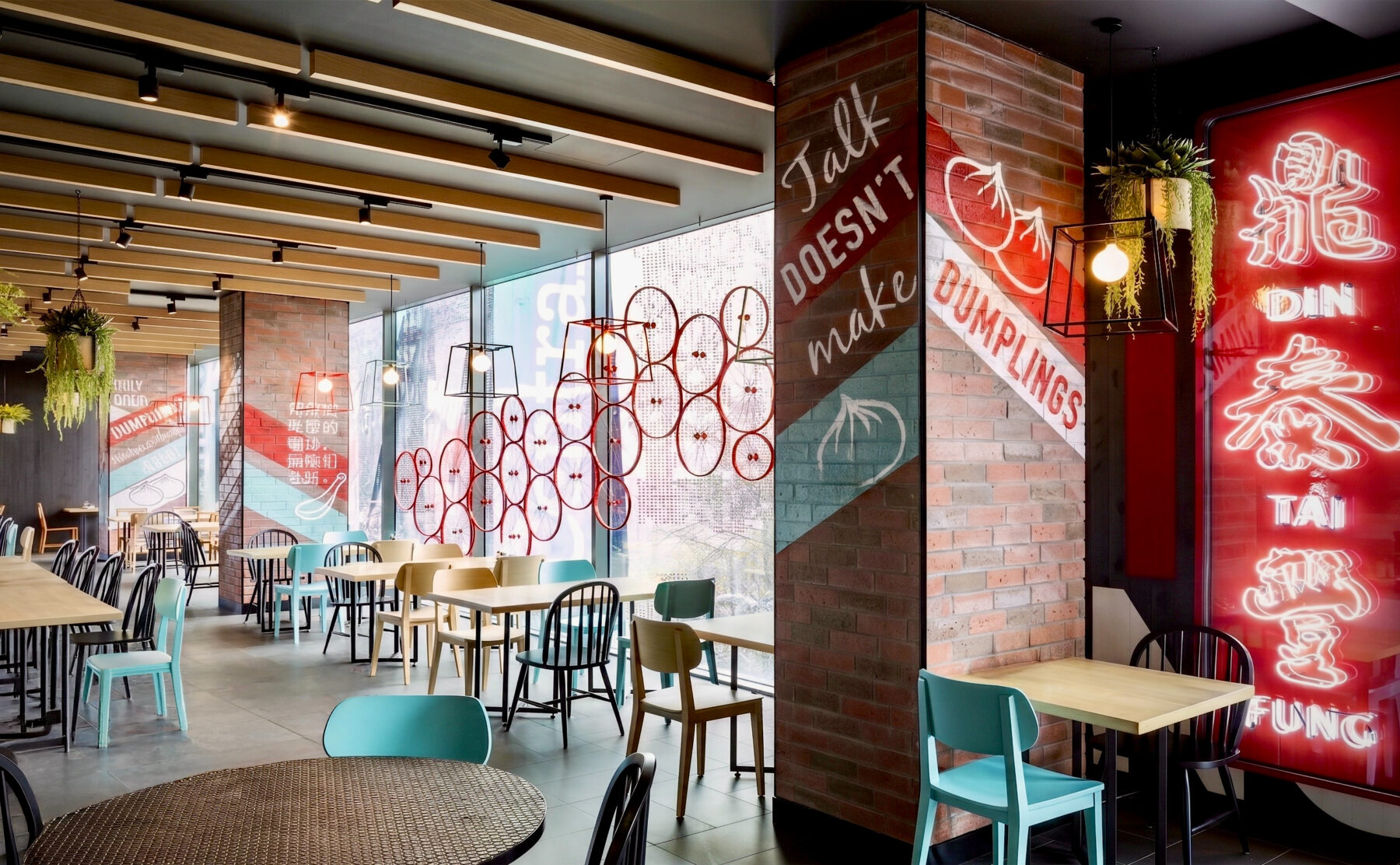 Restaurant dining area, vertical neon light box, brick columns with hand-painted graphics, timber ceiling beams, wire cage pendant lamps, mixed seating layout, window decals.