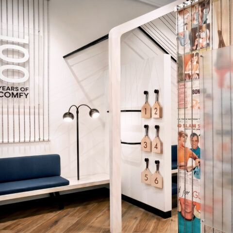 Retail changing rooms, timber flooring, upholstered bench seating, dimensional wall signage, heritage graphic curtains, minimalist floor lamps, commercial fit-out.