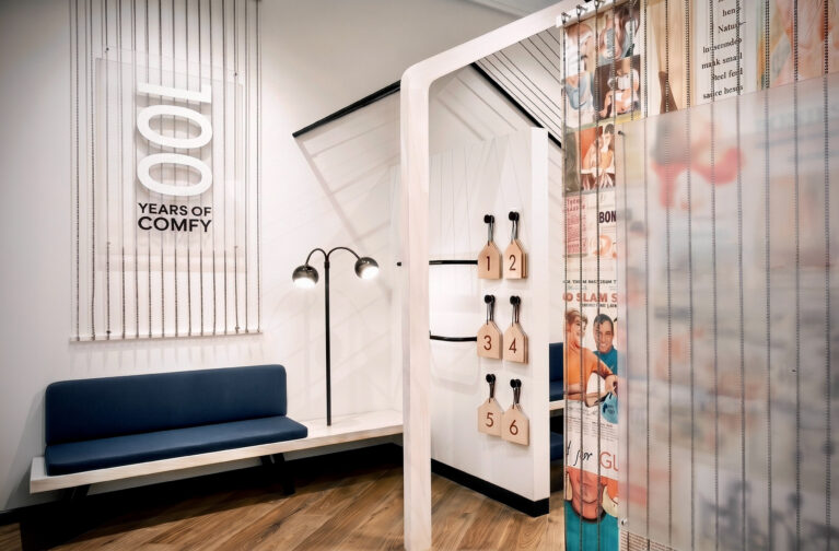 Retail changing rooms, timber flooring, upholstered bench seating, dimensional wall signage, heritage graphic curtains, minimalist floor lamps, commercial fit-out.