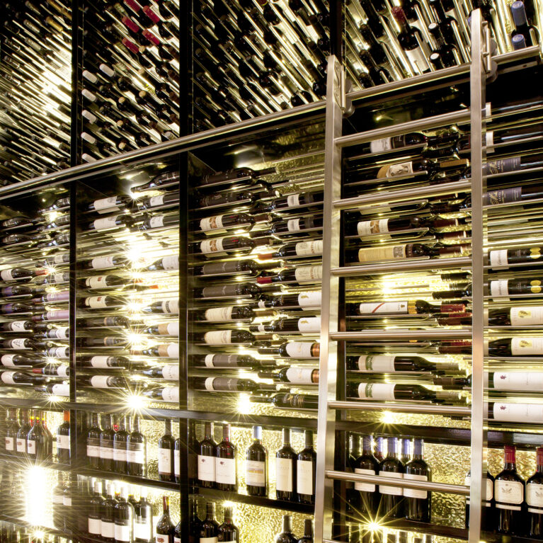 Bespoke wine display, floor-to-ceiling cellar shelves, integrated LED shelf lighting, rolling library ladder, stainless steel tracking, dark mirror backing, commercial hospitality joinery, luxury restaurant cellar.