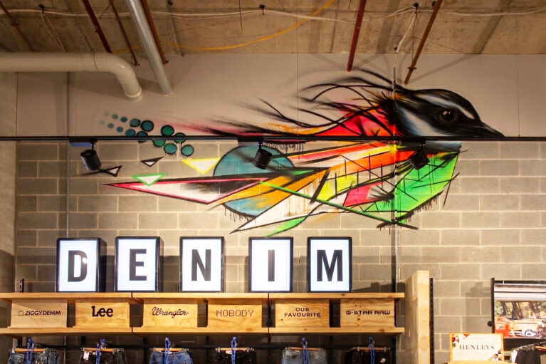 A retail denim display featuring a custom graffiti bird mural, exposed concrete blocks, illuminated 