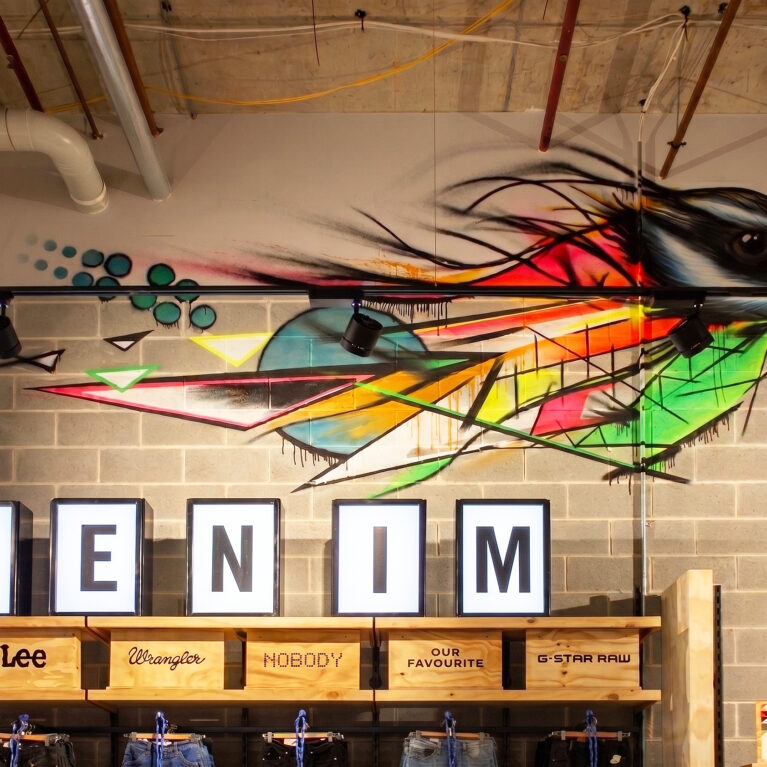 A retail denim display featuring a custom graffiti bird mural, exposed concrete blocks, illuminated 