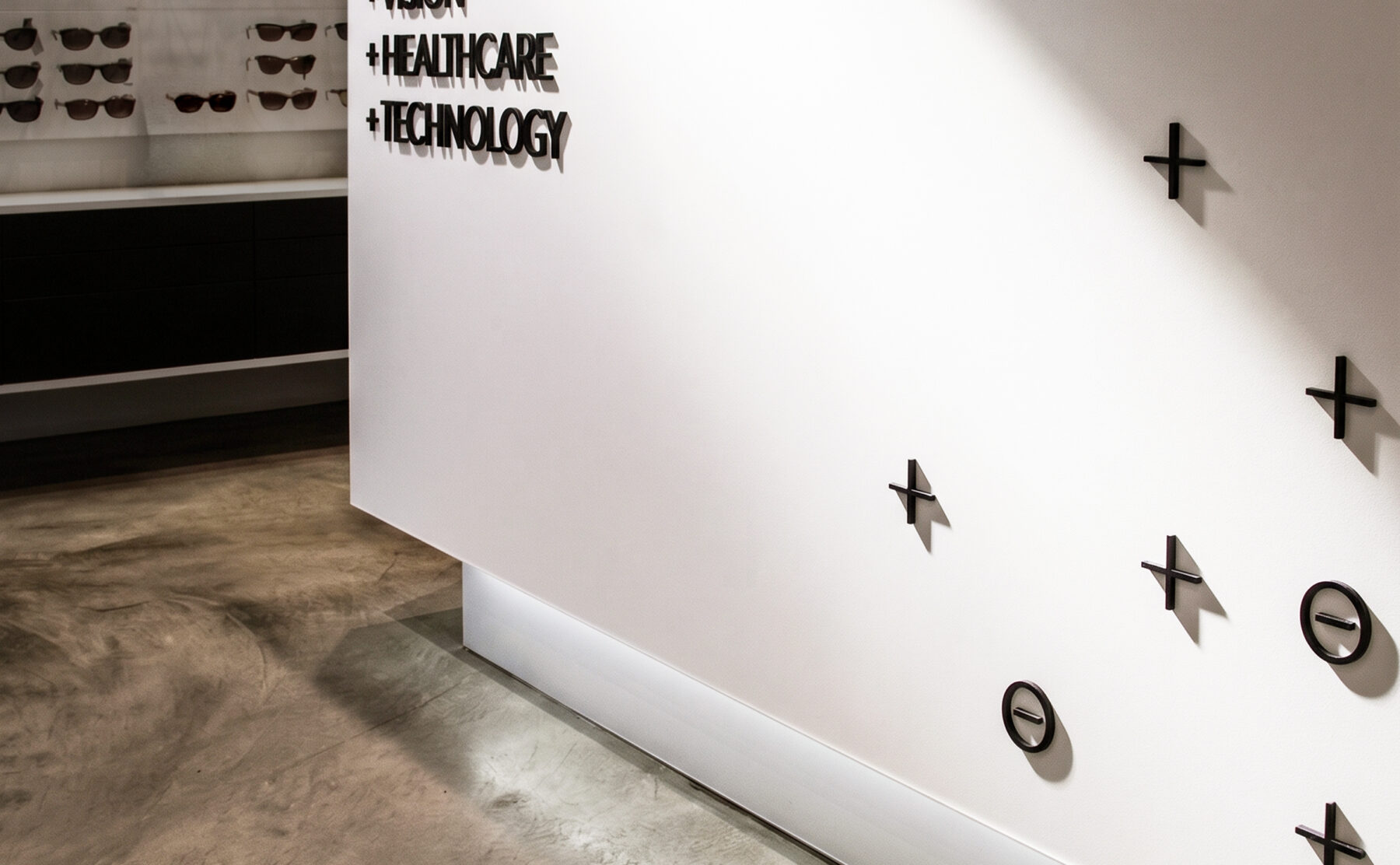 Optical retail reception counter, custom dimensional signage, seamless white solid surface, polished concrete floor, floating plinth lighting, sunglass display wall, minimalist medical interior.