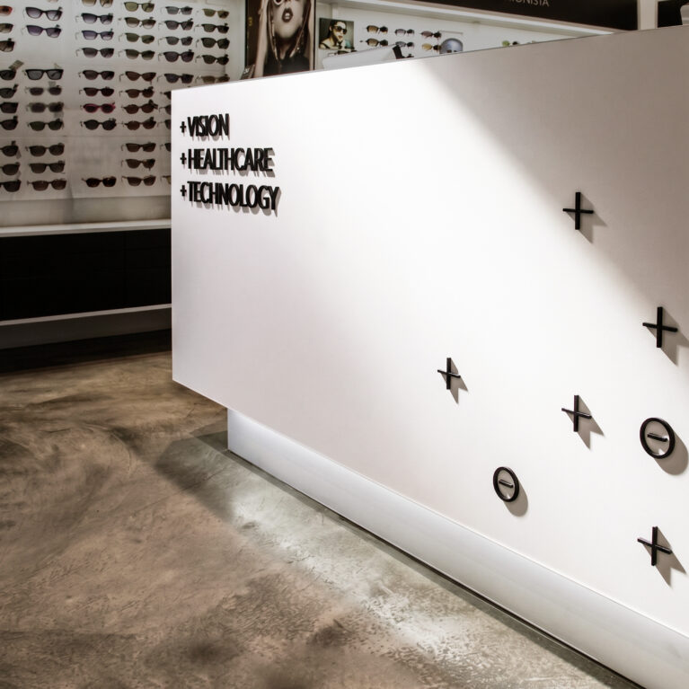 Optical retail reception counter, custom dimensional signage, seamless white solid surface, polished concrete floor, floating plinth lighting, sunglass display wall, minimalist medical interior.
