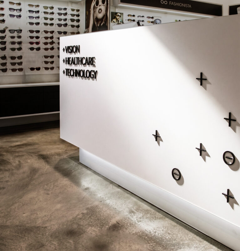 Optical retail reception counter, custom dimensional signage, seamless white solid surface, polished concrete floor, floating plinth lighting, sunglass display wall, minimalist medical interior.