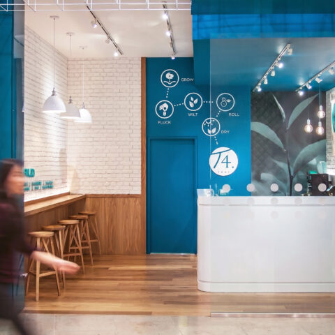 Shopping mall storefront, commercial tea shop facade, teal architectural bulkhead, glass retail partition, recessed ceiling downlights, wire frame installation, timber bar seating, open entrance layout.