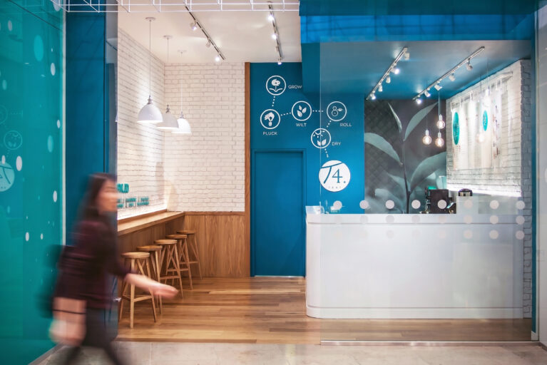 Shopping mall storefront, commercial tea shop facade, teal architectural bulkhead, glass retail partition, recessed ceiling downlights, wire frame installation, timber bar seating, open entrance layout.
