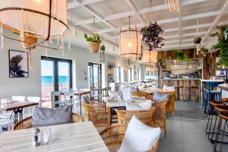 Bright dining interior featuring large-scale fabric pendants and open sea vistas.