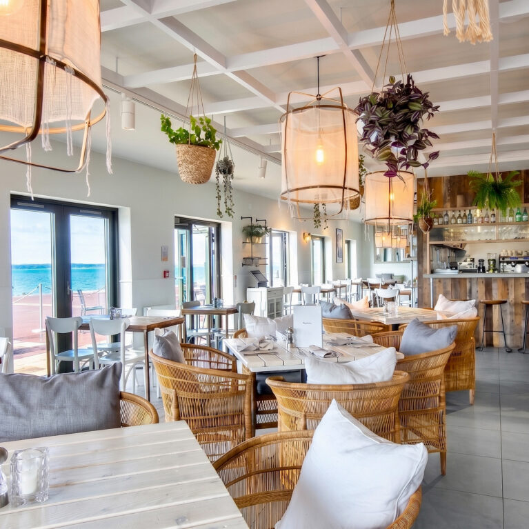 Bright dining interior featuring large-scale fabric pendants and open sea vistas.