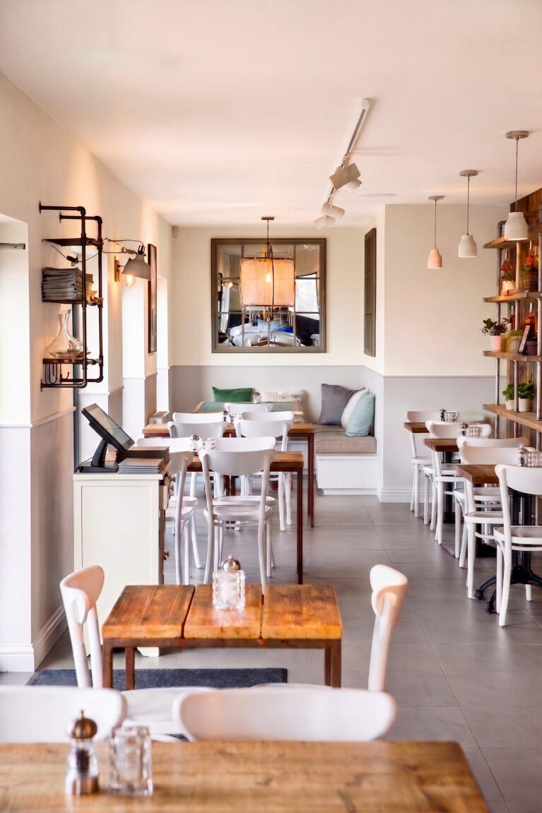 A deep interior viewpoint showcasing timber tables, white bentwood chairs, and a mirrored alcove.