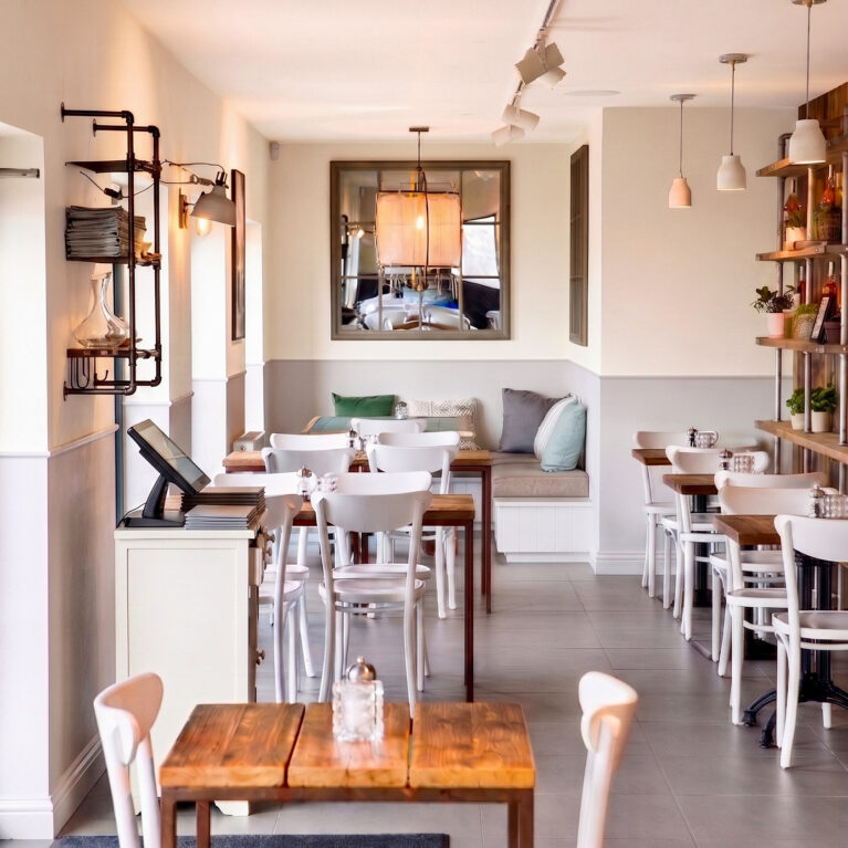 A deep interior viewpoint showcasing timber tables, white bentwood chairs, and a mirrored alcove.