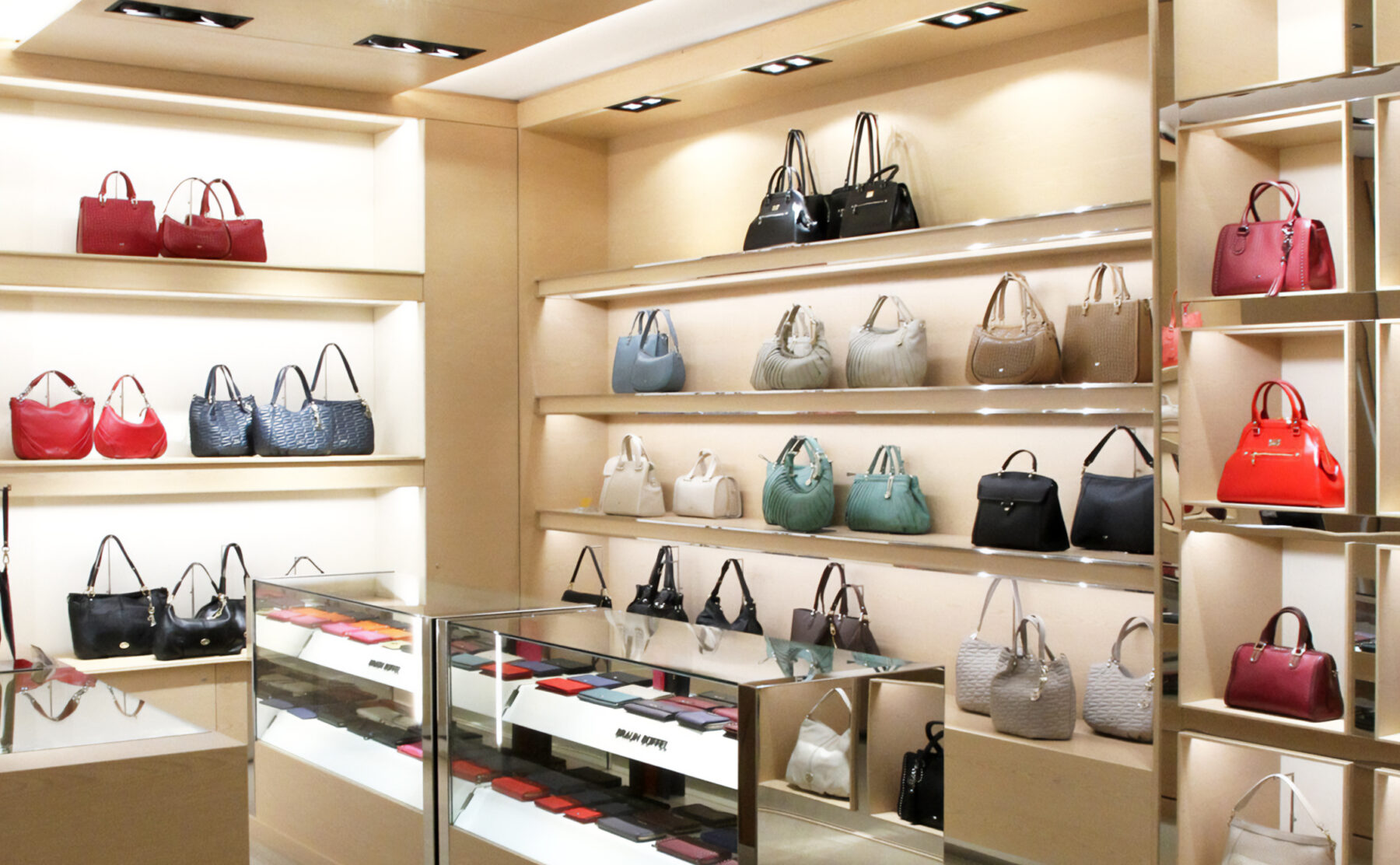Bespoke retail shelving, luxury handbag display, maple veneer joinery, integrated LED strip lights, glass counter showcase, polished steel trims, recessed ceiling downlights, premium retail layout.