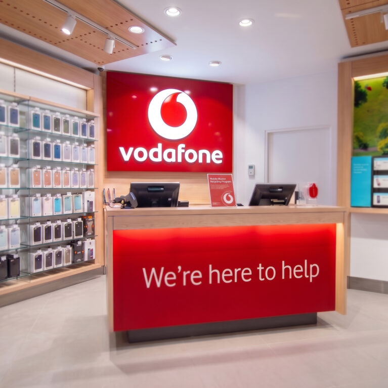 Another view of the Vodafone welcome desk, featuring vibrant signage and neatly arranged product displays.