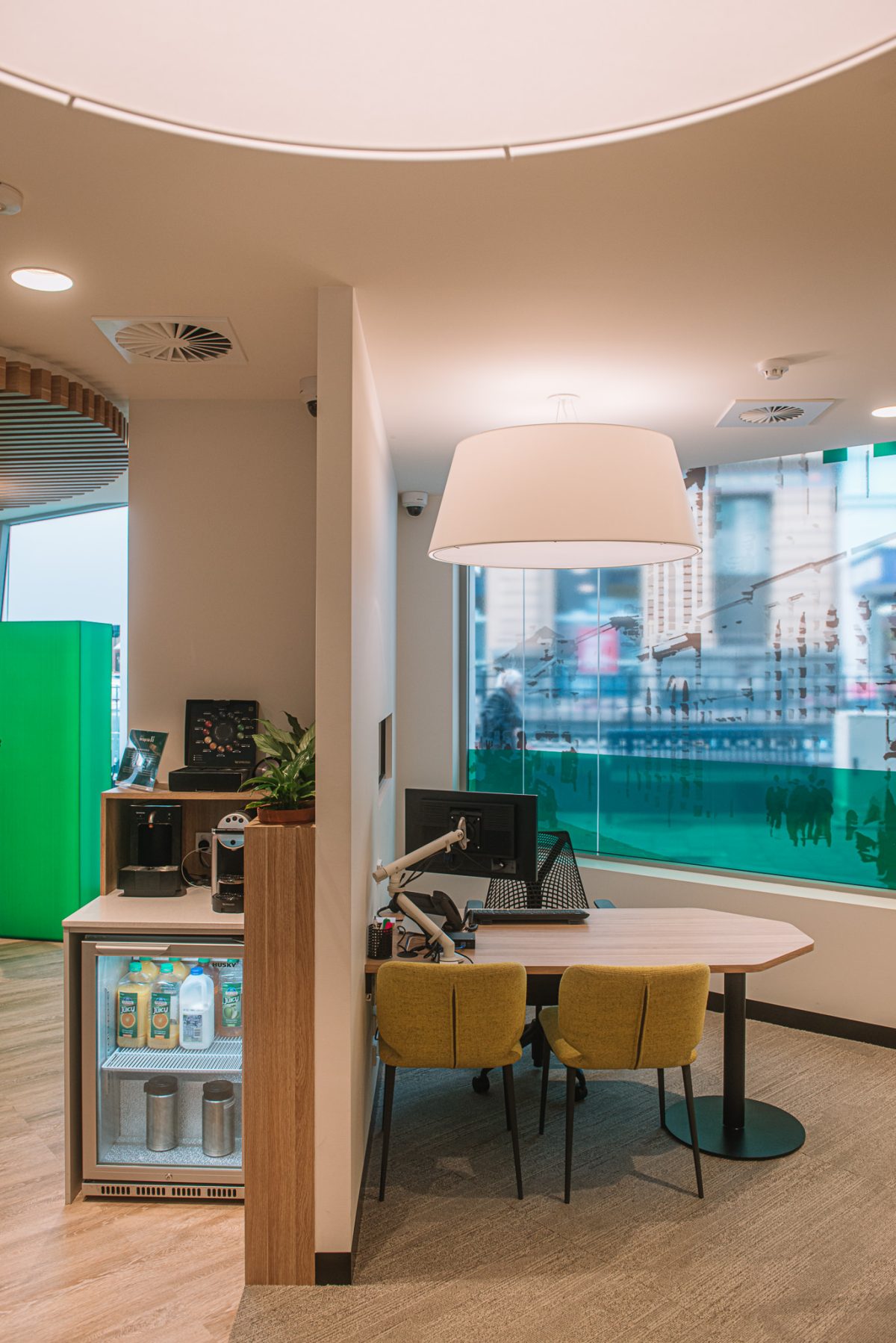 A modern, inviting workspace at Heritage Bank featuring a warm, contemporary design with light wood elements, mustard-toned chairs, and large windows offering city views.