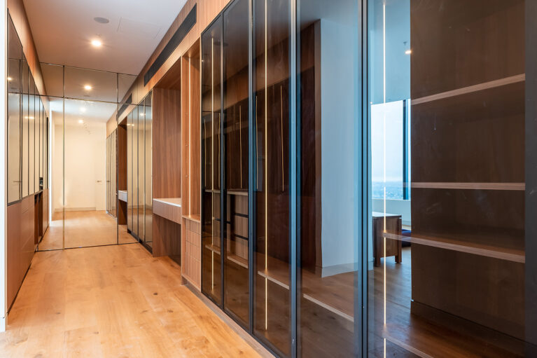 The walk-in closet hallway in the master suite features mirrored doors, open shelving, and rich wood finishes, creating a streamlined, elegant storage area with ample space for clothing and accessories.