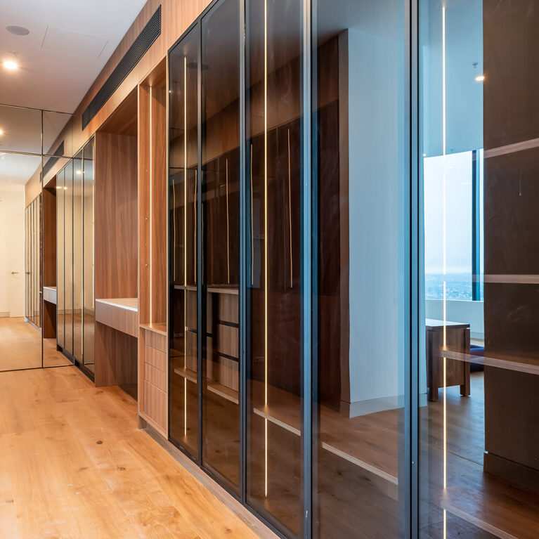 The walk-in closet hallway in the master suite features mirrored doors, open shelving, and rich wood finishes, creating a streamlined, elegant storage area with ample space for clothing and accessories.