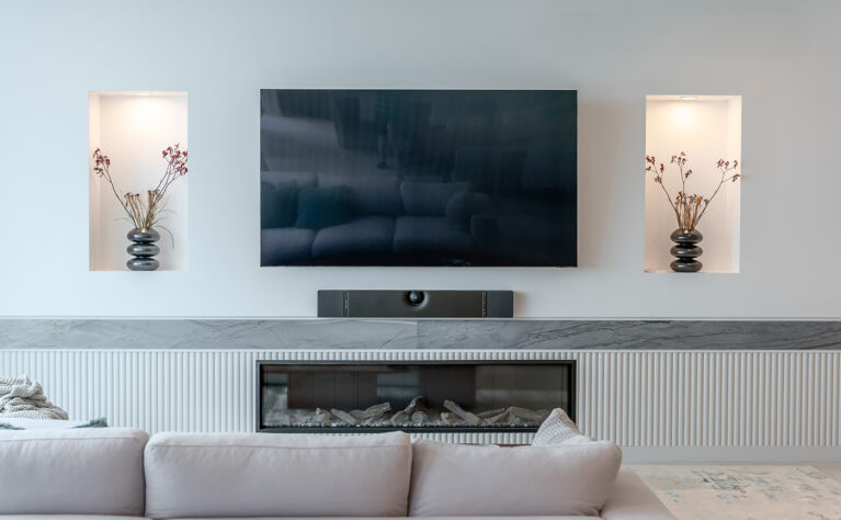 The living room’s entertainment wall combines function and style, with a minimalist design featuring a recessed TV, display niches, and a modern fireplace. 