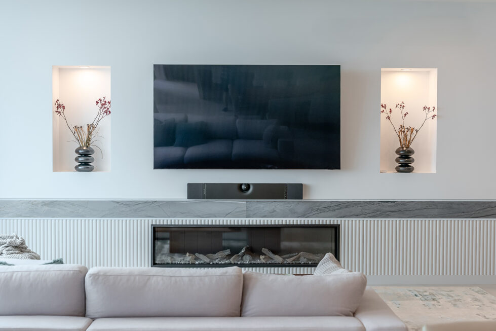 The living room’s entertainment wall combines function and style, with a minimalist design featuring a recessed TV, display niches, and a modern fireplace. 