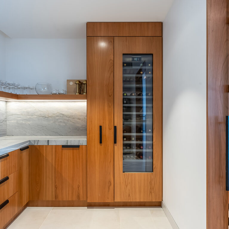 The butler’s pantry offers additional storage with a blend of glass-fronted and solid cabinets, providing both display space and concealed storage. The sleek wood finish ensures continuity with the main kitchen’s design.