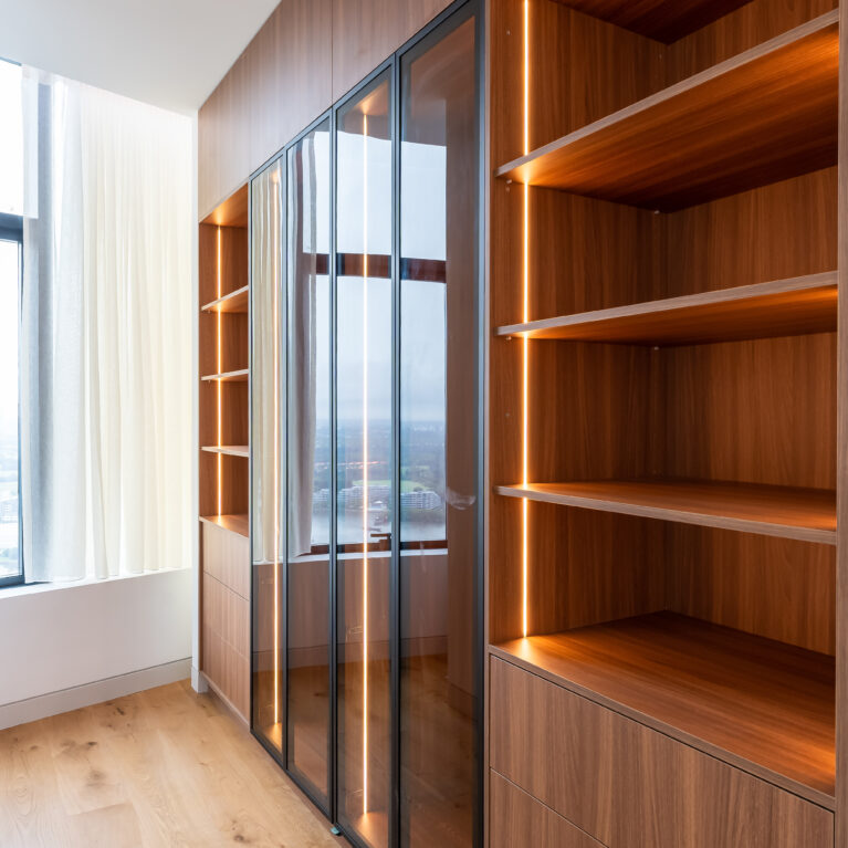 The master bedroom’s wardrobe offers streamlined storage with glass-fronted cabinets and warm lighting. This elegant space combines functionality and style, keeping essentials organized while adding a touch of sophistication.