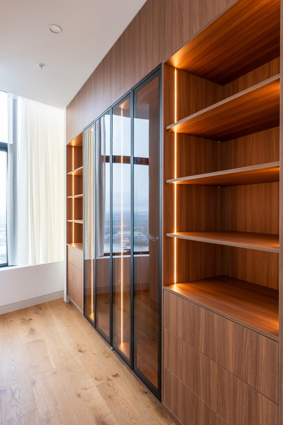 The master bedroom’s wardrobe offers streamlined storage with glass-fronted cabinets and warm lighting. This elegant space combines functionality and style, keeping essentials organized while adding a touch of sophistication.