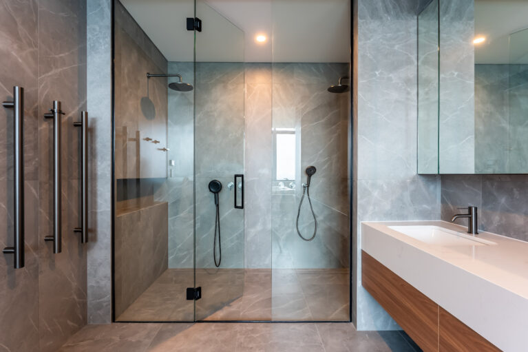 The master ensuite’s double shower provides a luxurious experience, with dual rain showerheads, gray stone tiles, and glass doors. This spacious design combines functionality with a high-end aesthetic for ultimate comfort.