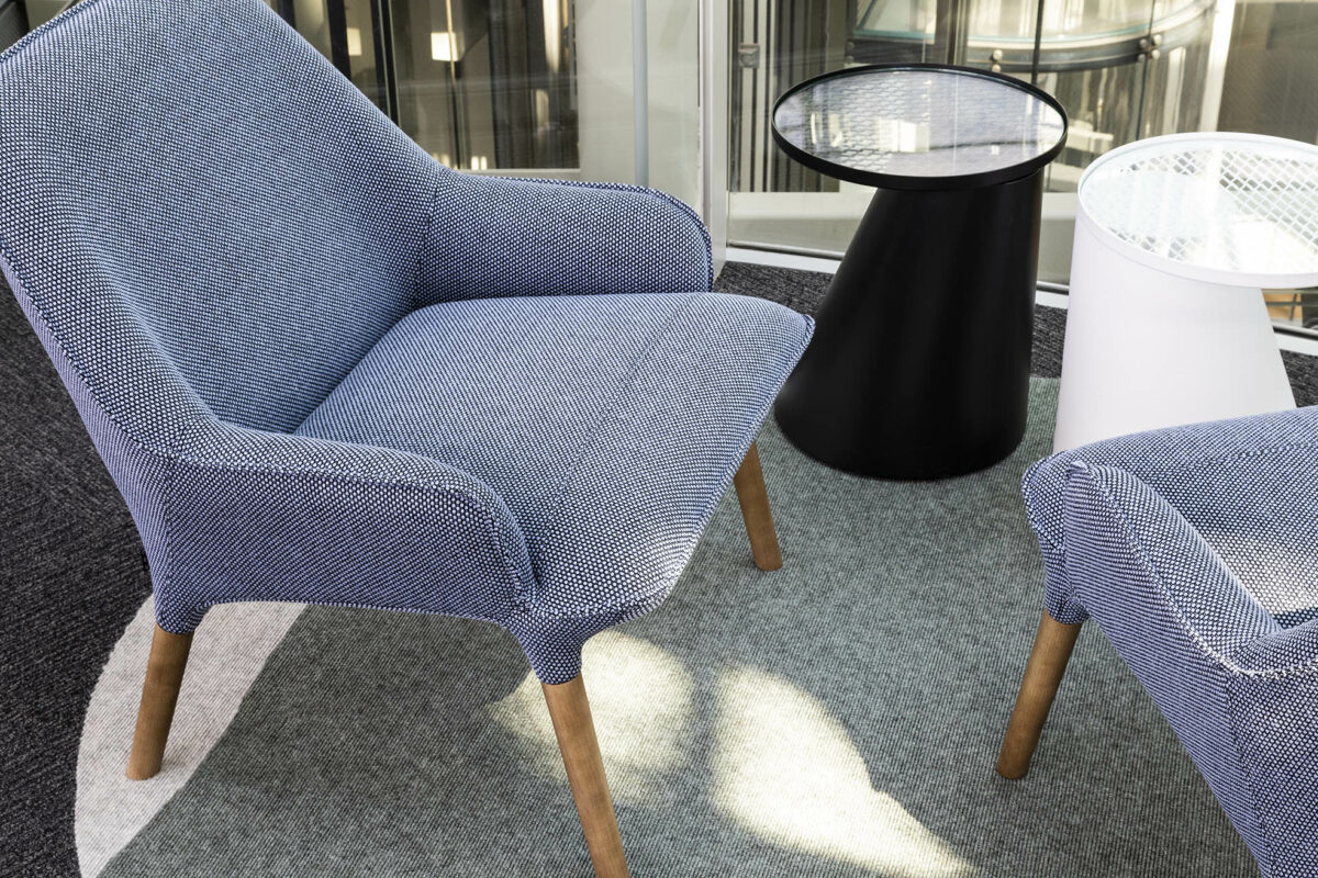 Soft blue upholstered seating flanked by low tables offers moments of pause in the workspace, ideal for quick chats, screen breaks or quiet reflection amid the flow of activity.
