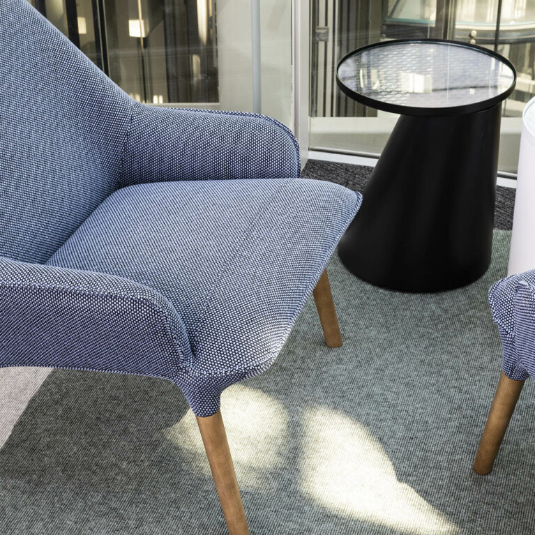 Soft blue upholstered seating flanked by low tables offers moments of pause in the workspace, ideal for quick chats, screen breaks or quiet reflection amid the flow of activity.