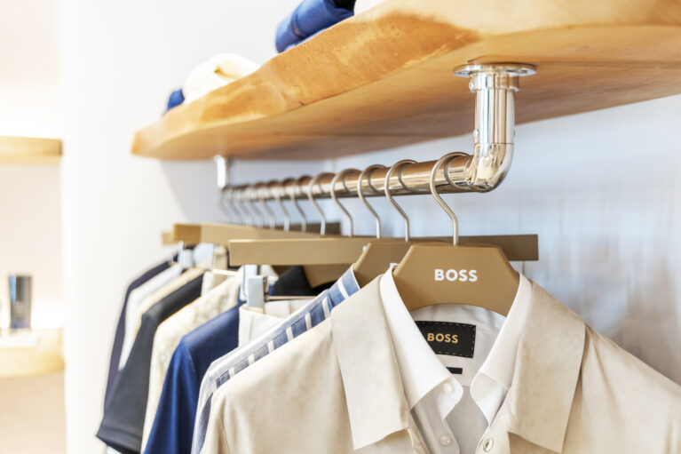 The clothing display balances sophistication and natural elements, featuring solid wood shelves, polished metal fixtures, and custom-branded hangers. The blend of organic textures and sleek finishes enhances the boutique’s contemporary yet relaxed aesthetic.