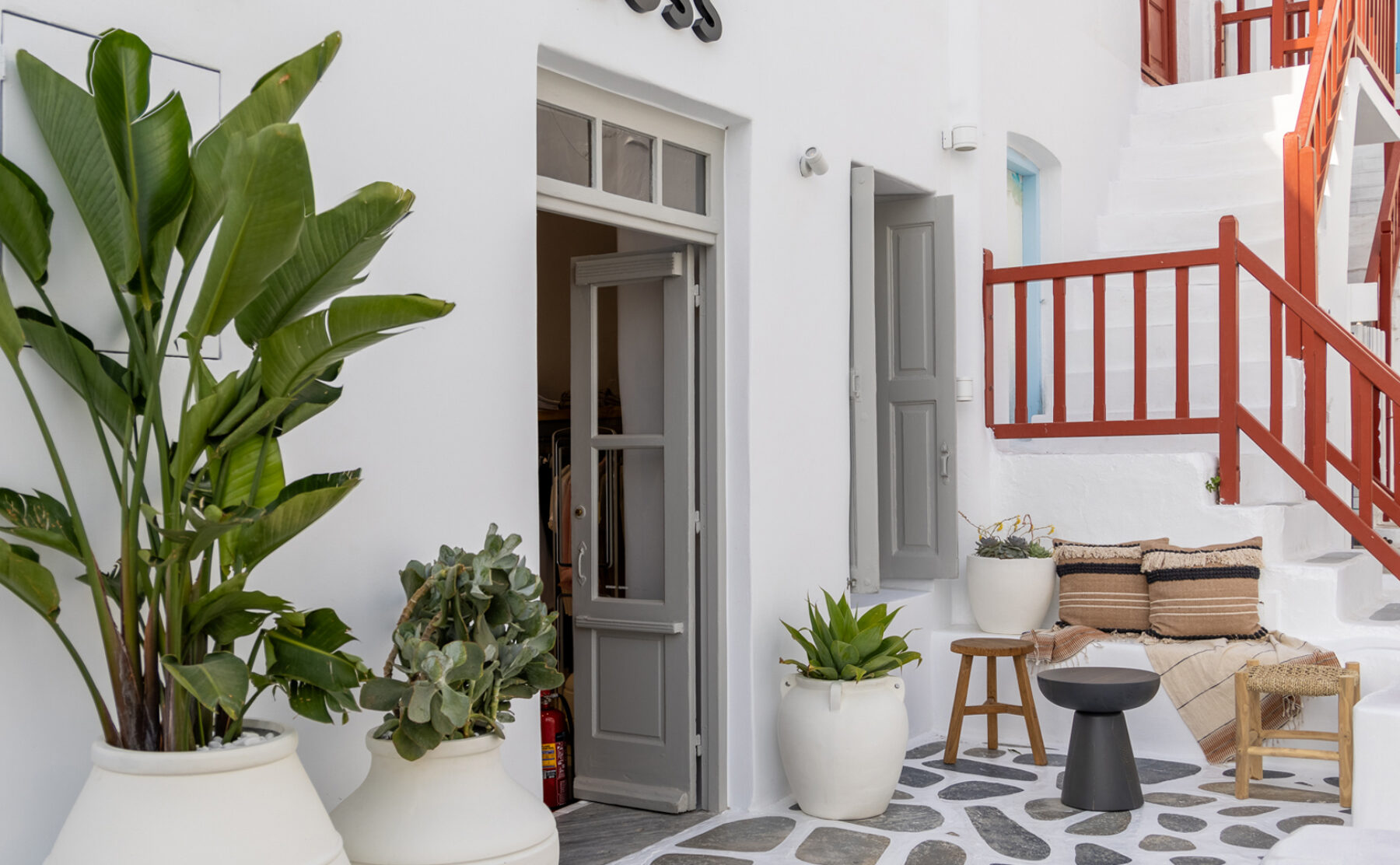 A serene courtyard invites guests to relax with its mix of natural textures, neutral tones, and lush greenery. Woven furniture and soft textiles blend seamlessly with the traditional whitewashed architecture, creating a sophisticated yet laid-back Mediterranean atmosphere.