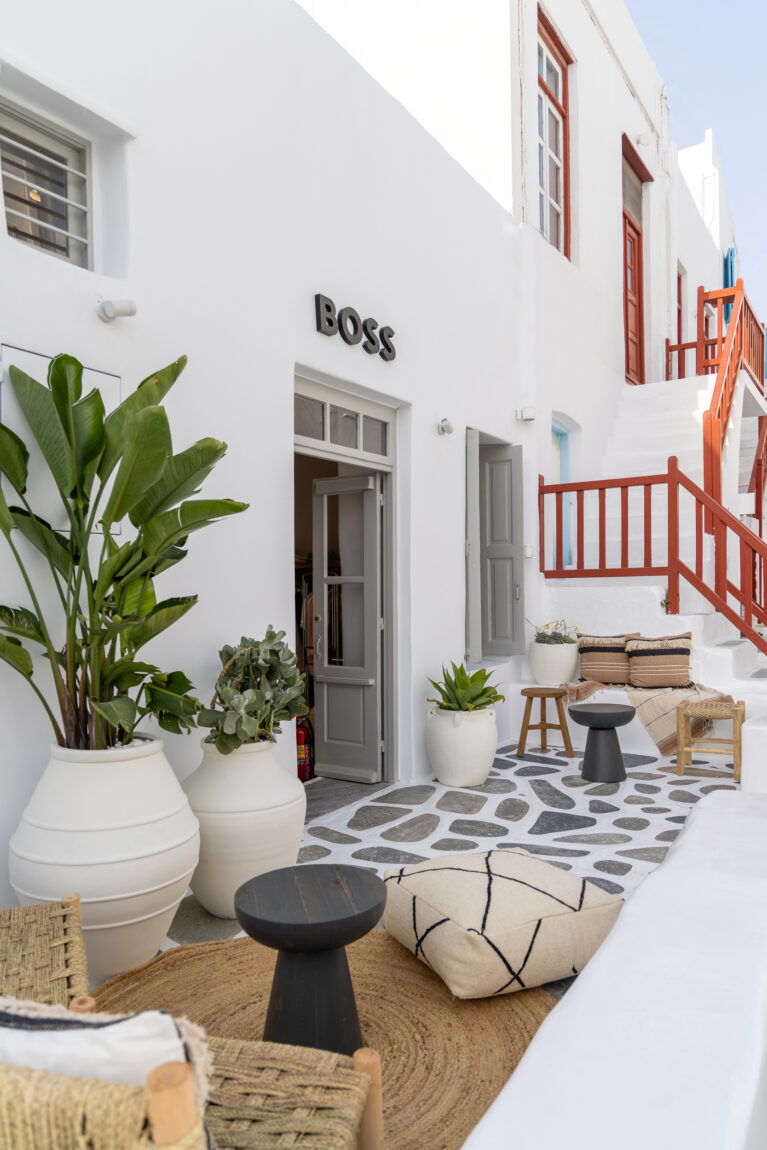 A serene courtyard invites guests to relax with its mix of natural textures, neutral tones, and lush greenery. Woven furniture and soft textiles blend seamlessly with the traditional whitewashed architecture, creating a sophisticated yet laid-back Mediterranean atmosphere.