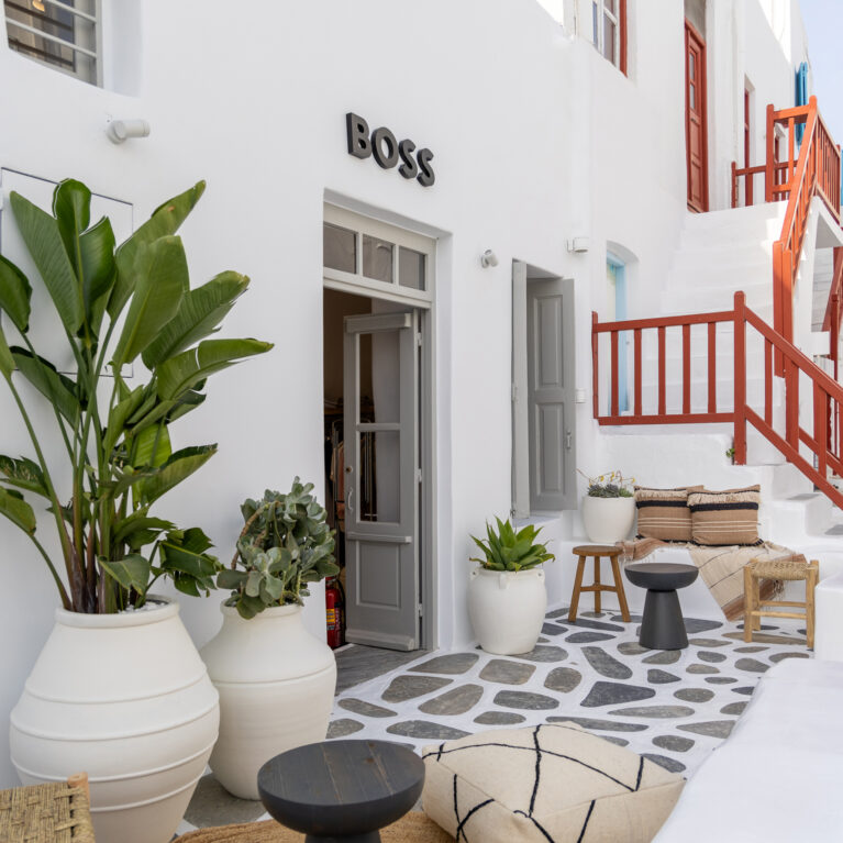 A serene courtyard invites guests to relax with its mix of natural textures, neutral tones, and lush greenery. Woven furniture and soft textiles blend seamlessly with the traditional whitewashed architecture, creating a sophisticated yet laid-back Mediterranean atmosphere.