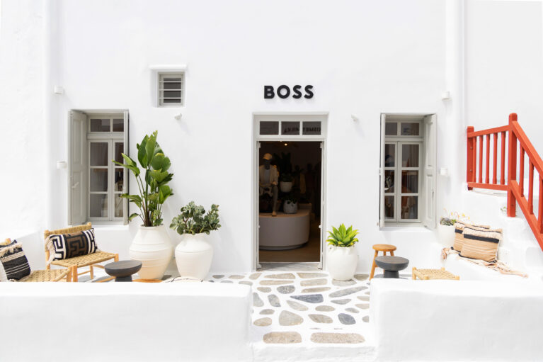 The entrance to the Boss pop-up store in Mykonos exudes a sophisticated yet relaxed aesthetic. The crisp white façade, stone-paved patio, and natural textures create a harmonious balance between Cycladic tradition and modern elegance, welcoming visitors into a refined retail experience.